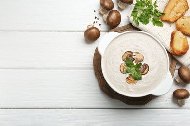 Photo of Delicious homemade mushroom soup in ceramic pot, croutons, fresh champignons and parsley on white wooden table, flat lay. Space for text
