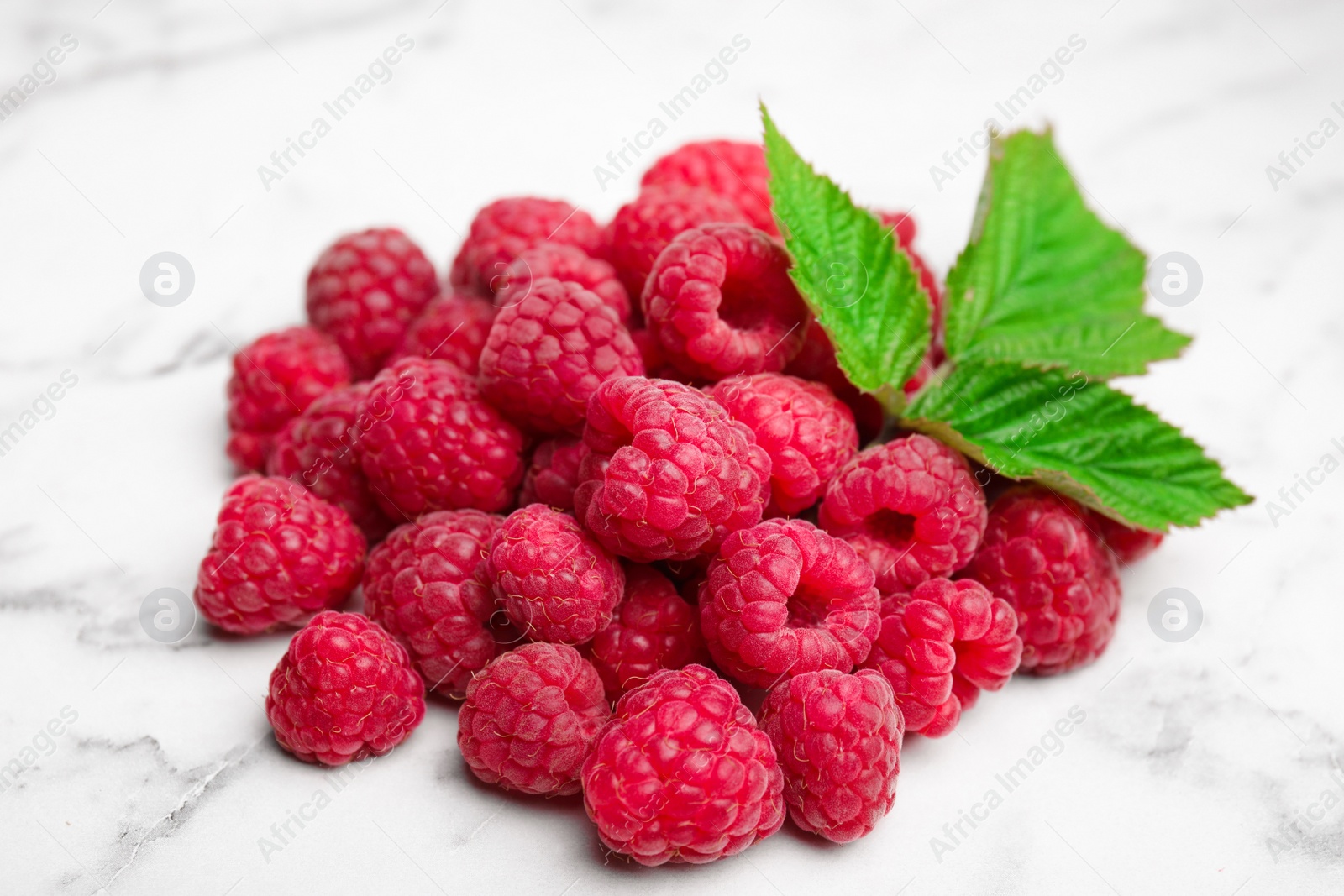 Photo of Fresh ripe raspberries with green leaves on white marble table