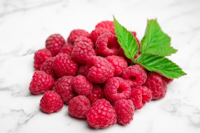 Fresh ripe raspberries with green leaves on white marble table