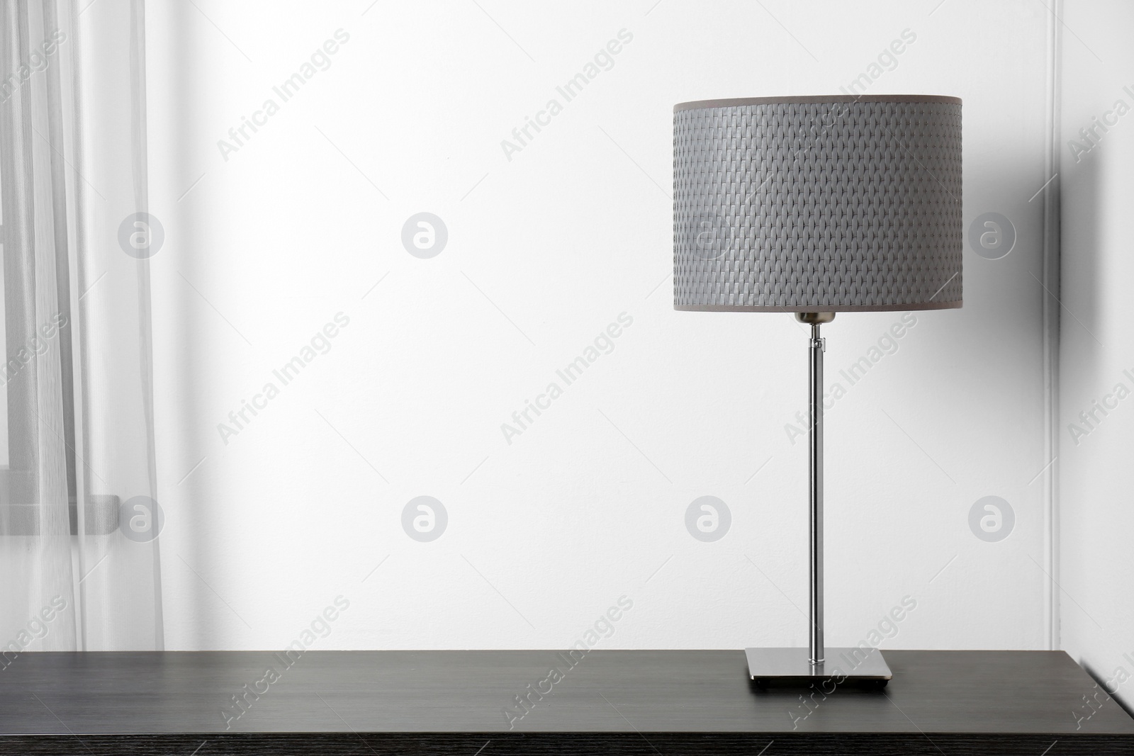 Photo of Stylish lamp on table near white wall. Space for text