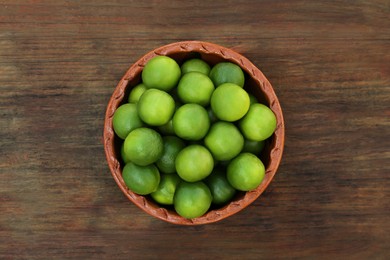 Photo of Fresh ripe limes in bowl on wooden table, top view