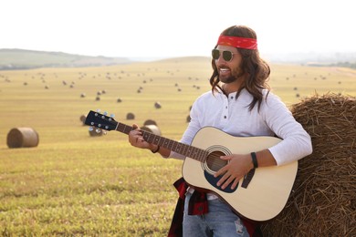 Photo of Hippie man playing guitar near hay bale in field