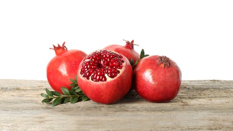 Photo of Fresh pomegranates and green leaves on wooden table against white background