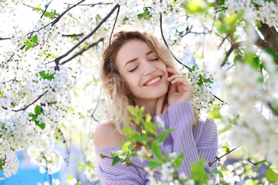 Photo of Attractive young woman posing near blossoming tree on sunny spring day