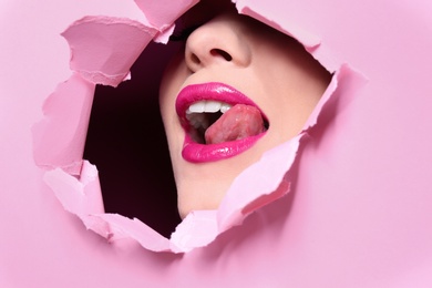 Photo of View of beautiful young woman with perfect lips makeup through hole in color paper