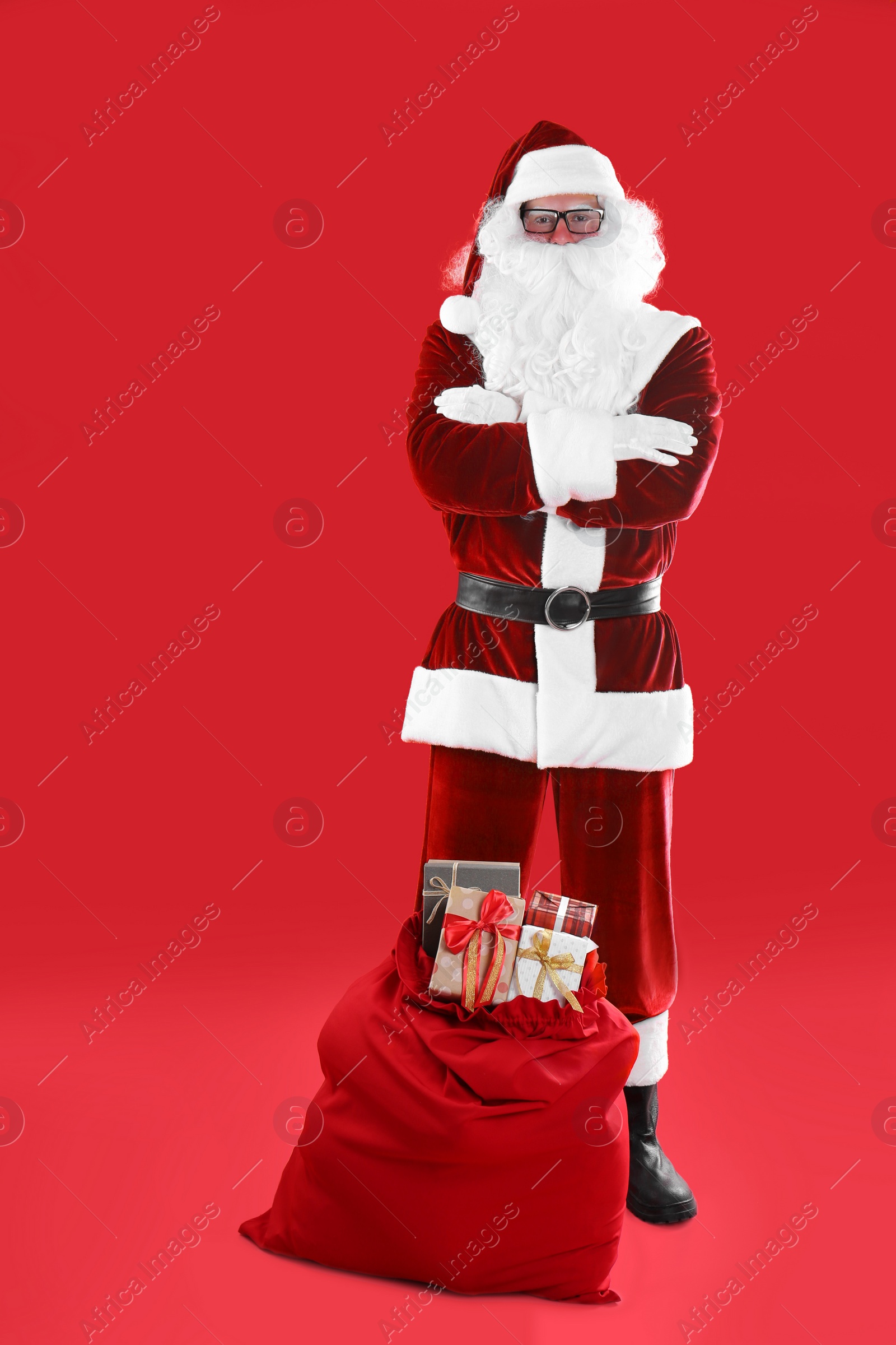 Photo of Santa Claus near sack with gift boxes on red background