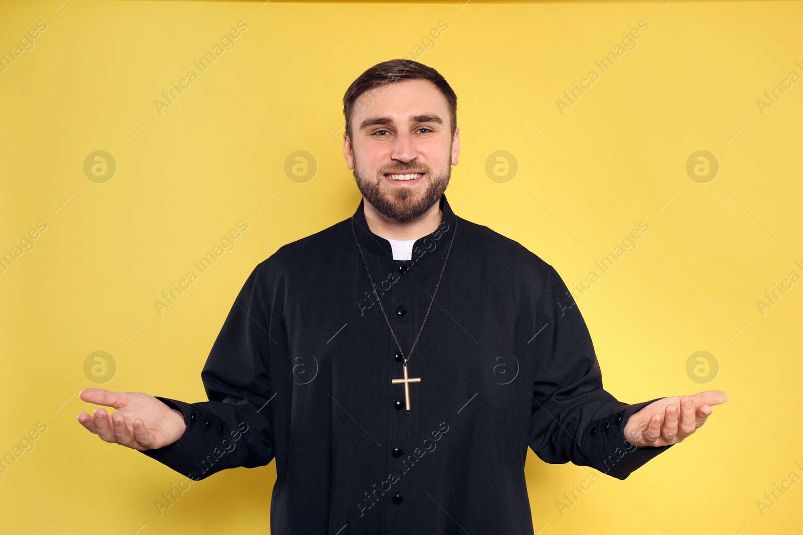 Photo of Priest wearing cassock with clerical collar on yellow background