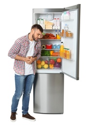 Young man feeling sick near open refrigerator on white background