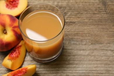 Photo of Glass of peach juice and fresh fruits on wooden table, closeup. Space for text