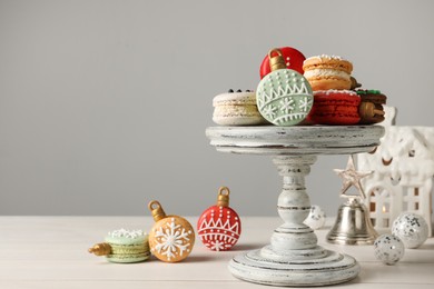 Photo of Stand with beautifully decorated Christmas macarons on white wooden table, space for text