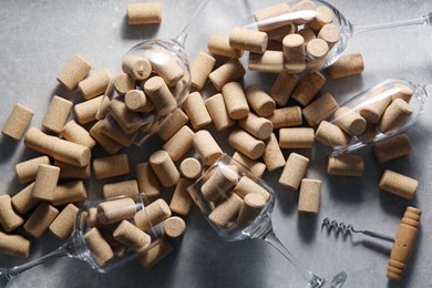 Photo of Glasses with many wine corks and corkscrew on light grey table, flat lay