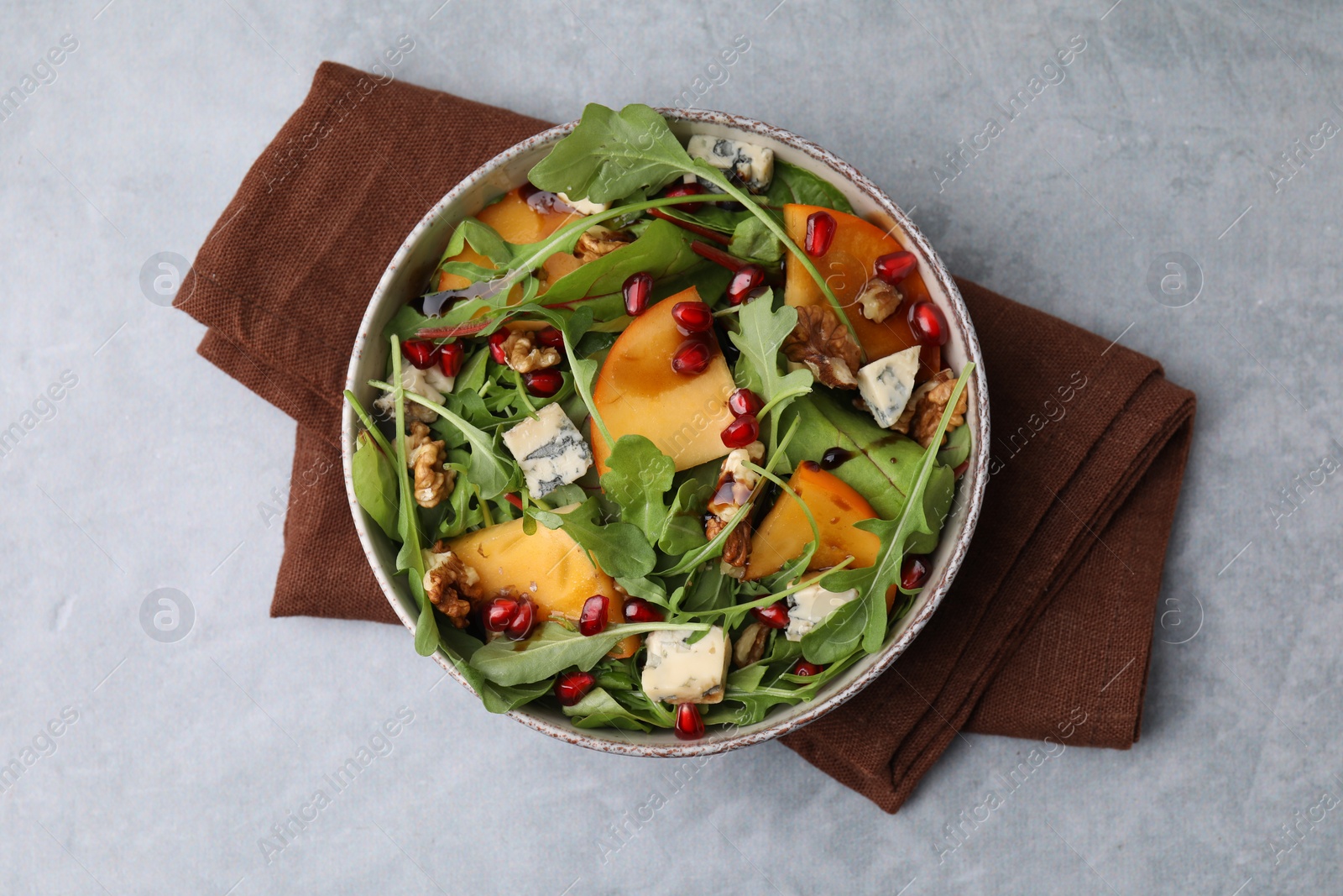 Photo of Tasty salad with persimmon, blue cheese, pomegranate and walnuts served on light grey table, top view