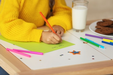 Photo of Little child writing letter to Santa at table indoors, closeup. Christmas season