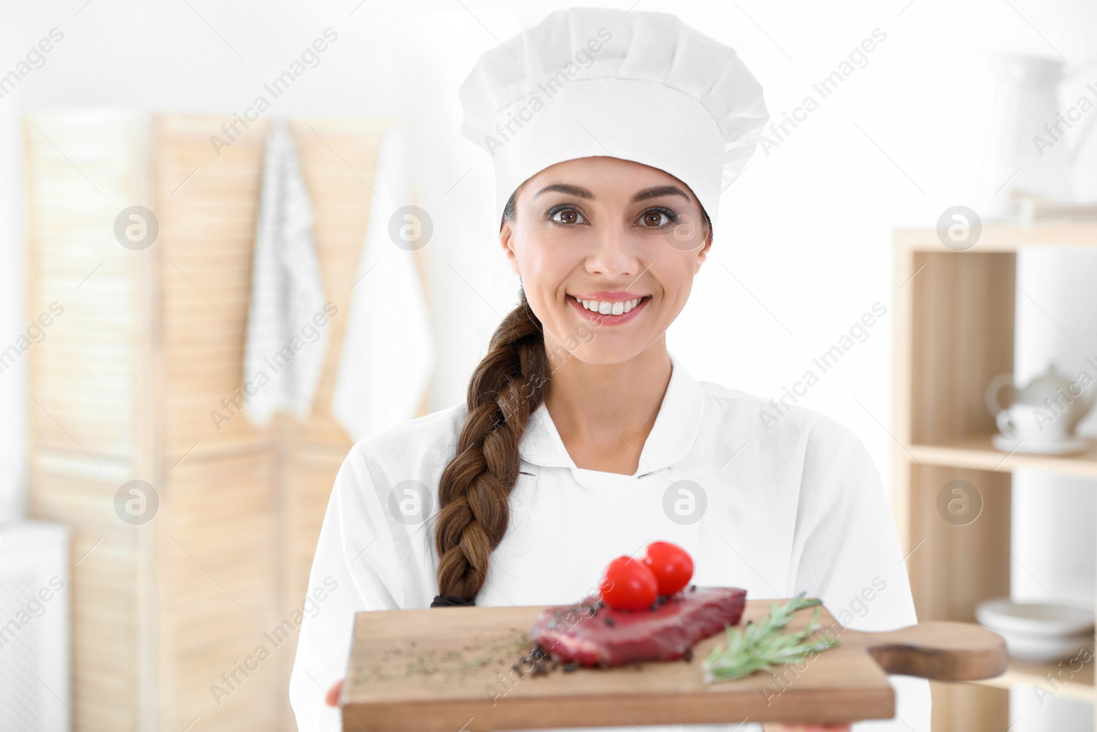 Photo of Professional female chef holding board with meat in kitchen