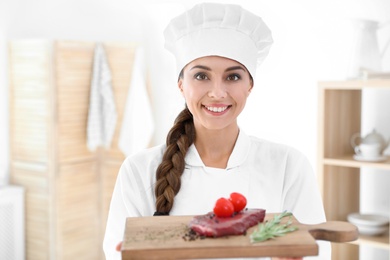 Professional female chef holding board with meat in kitchen