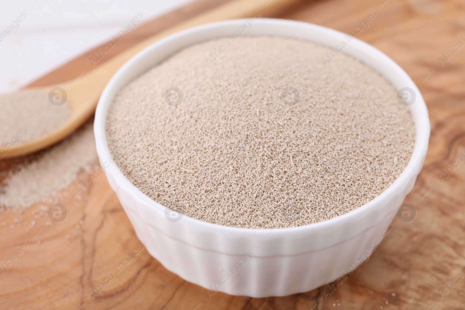 Photo of Bowl and spoon with active dry yeast on wooden board, closeup