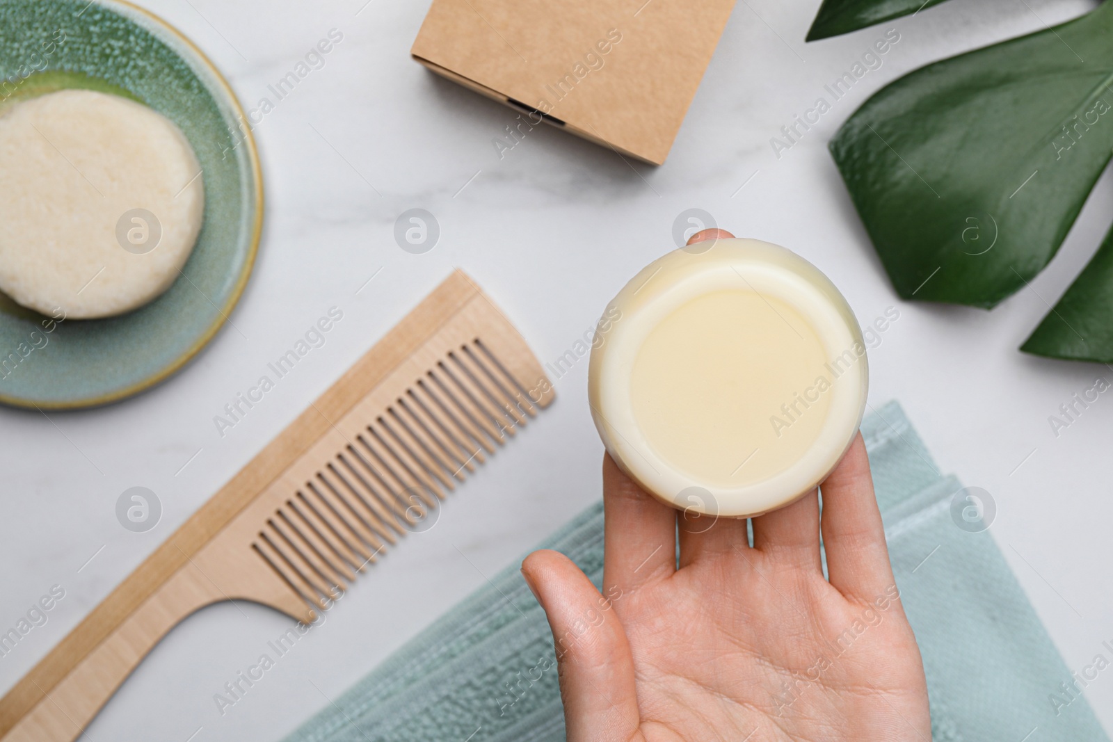 Photo of Woman holding solid shampoo bar at marble table, top view. Hair care