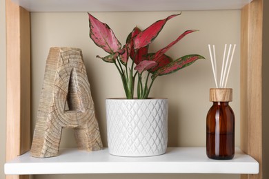 Photo of Aromatic reed air freshener near houseplant on white shelf