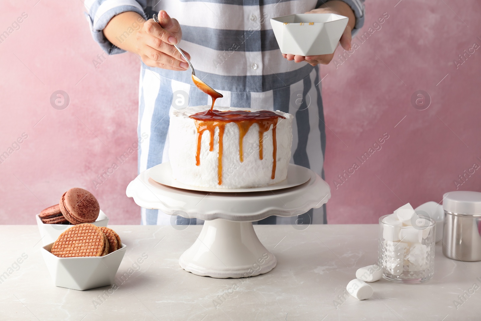 Photo of Young woman applying caramel sauce onto delicious homemade cake at table