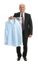 Senior man holding hanger with shirt in plastic bag on white background. Dry-cleaning service