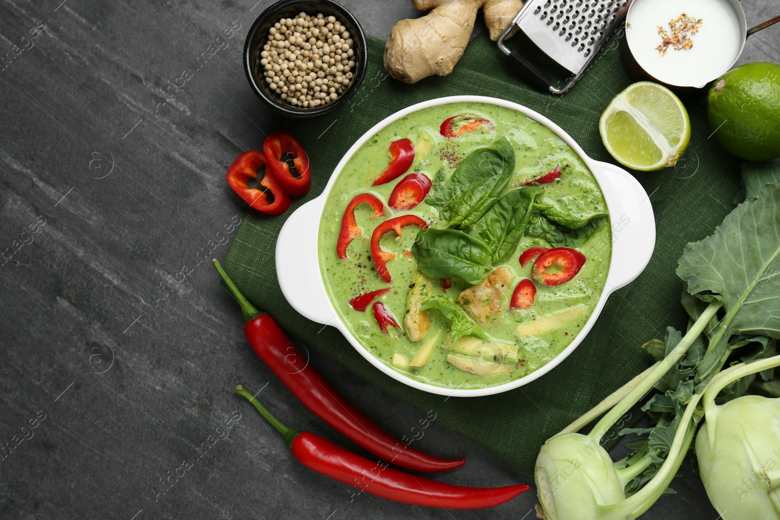 Photo of Saucepan with delicious green curry chicken soup and different ingredients on grey table, flat lay. Space for text