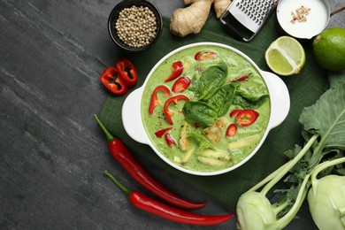 Saucepan with delicious green curry chicken soup and different ingredients on grey table, flat lay. Space for text