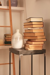 Photo of Stack of different books and vase on table near bookshelves in home library