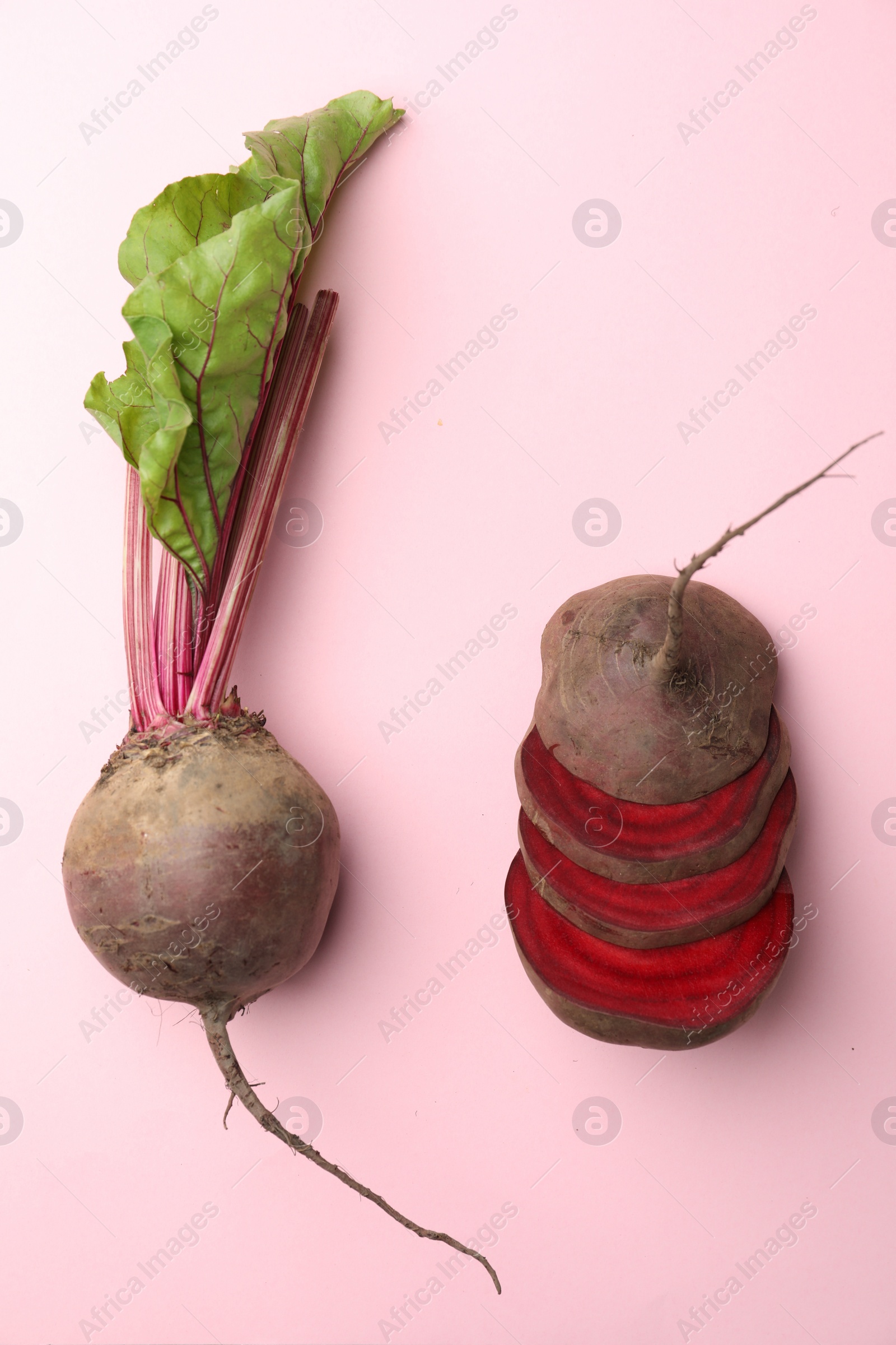 Photo of Whole and cut fresh red beets on pink background, flat lay