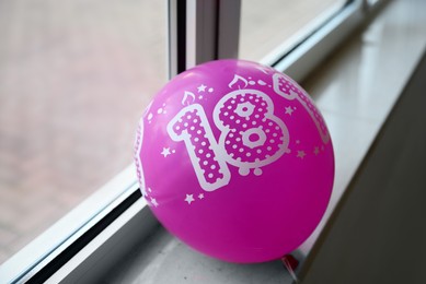 Pink balloon with number 18 as birthday candles on windowsill indoors. Coming of age party