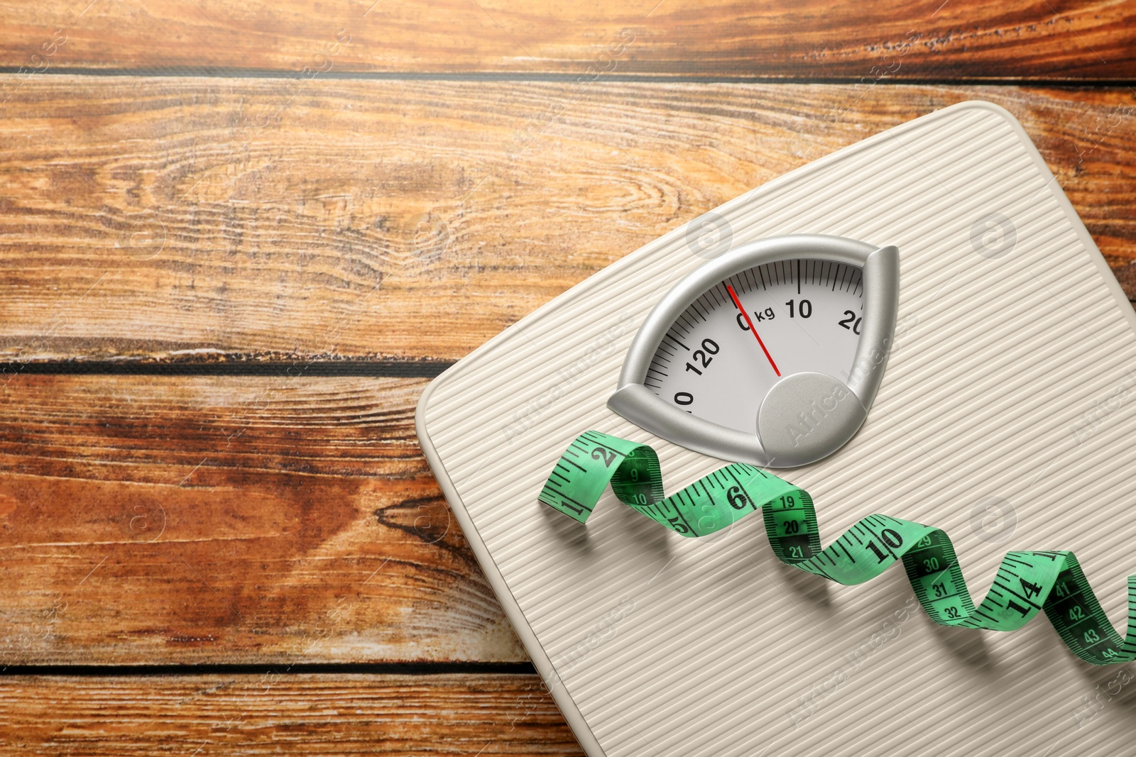 Photo of Weigh scales with measuring tape on wooden table, top view and space for text. Overweight concept