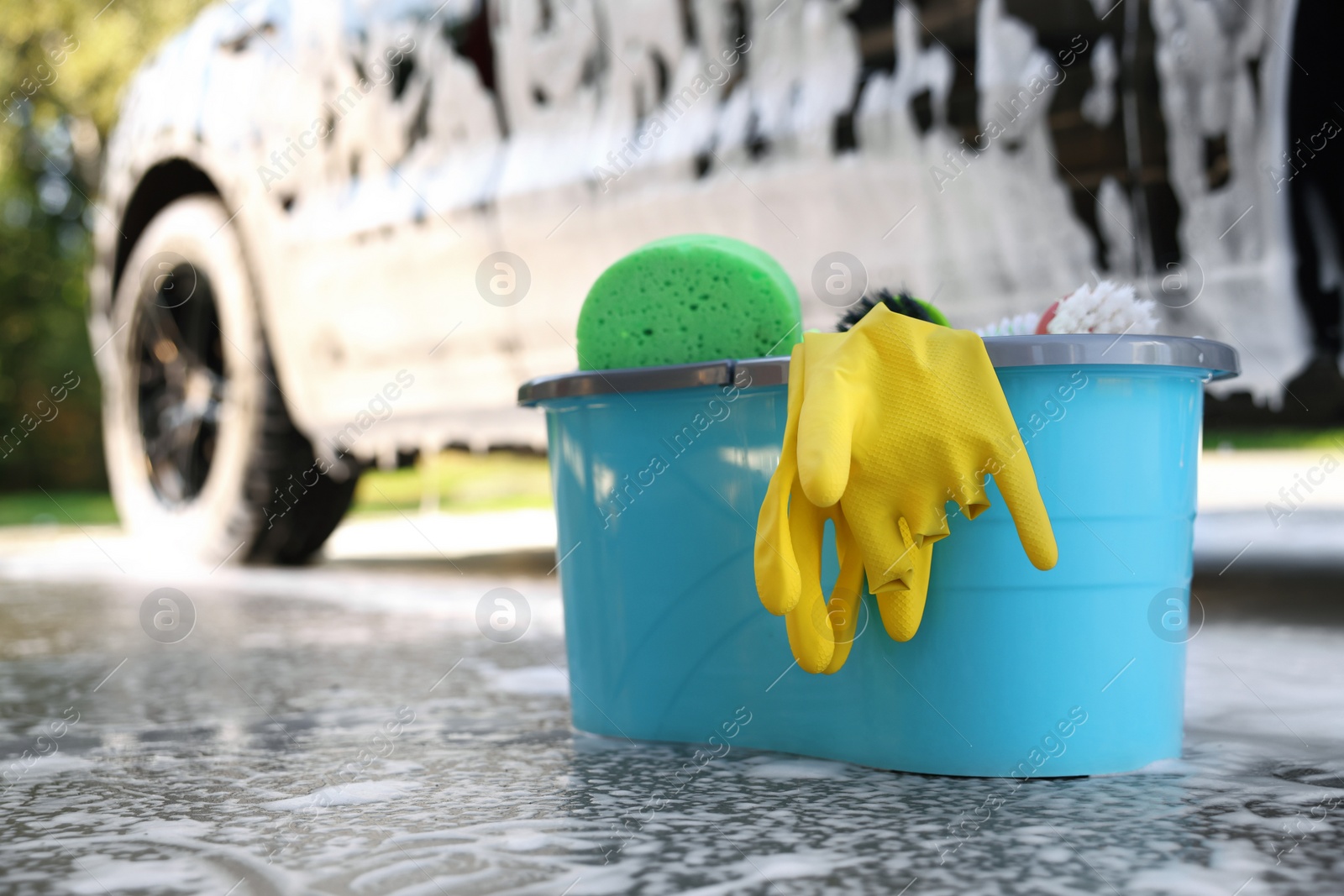 Photo of Car cleaning supplies and auto covered with foam outdoors