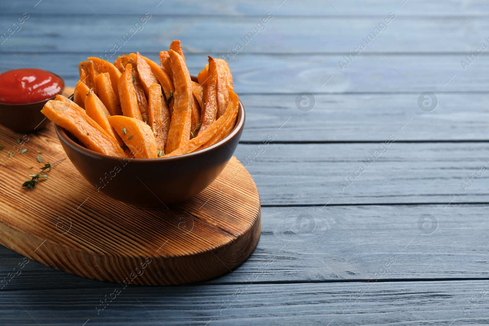 Photo of Bowl with tasty sweet potato fries on wooden background, space for text