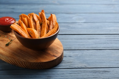 Bowl with tasty sweet potato fries on wooden background, space for text