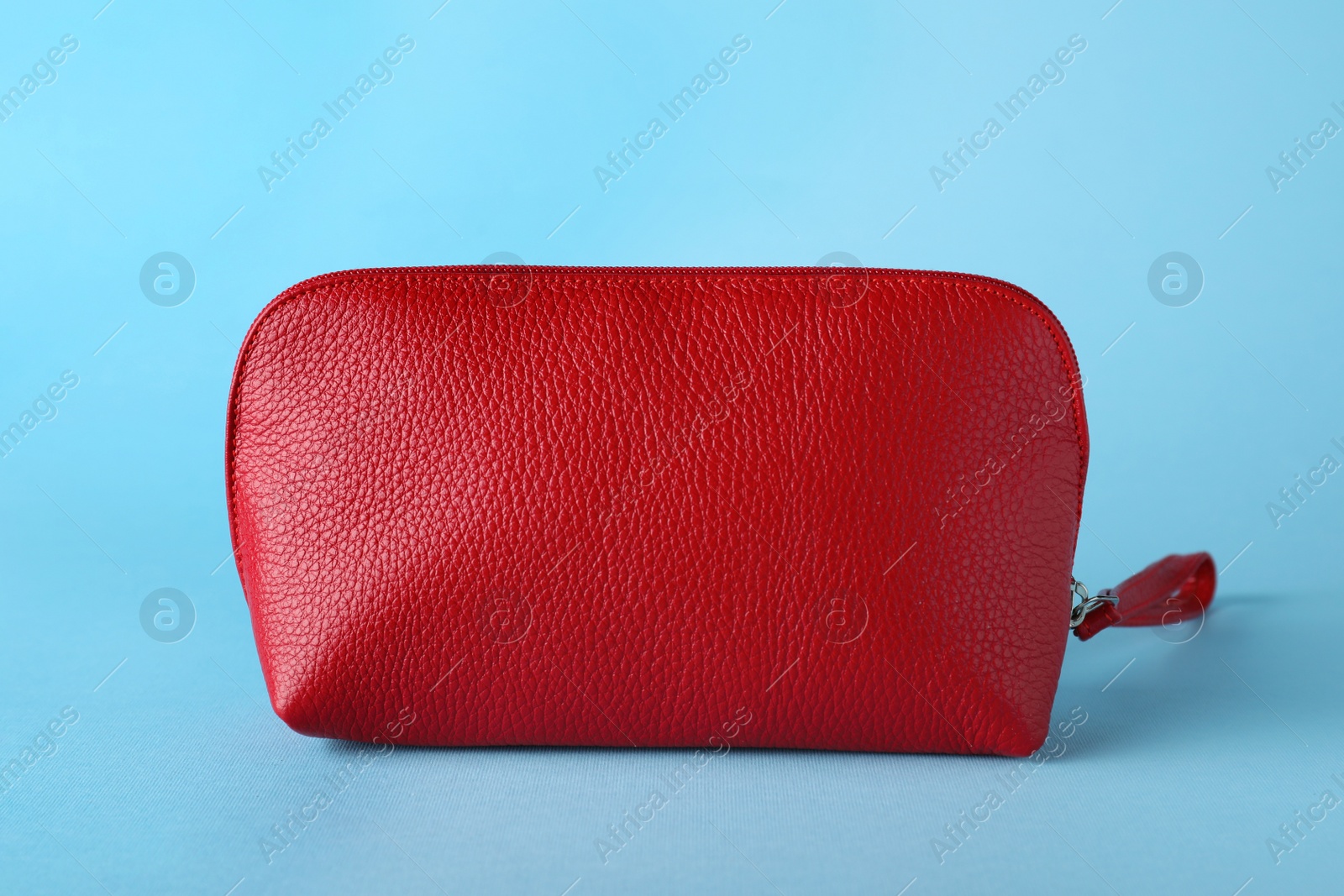 Photo of Red leather cosmetic bag on light blue background, closeup
