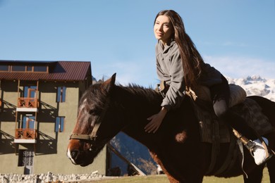 Photo of Young woman riding horse in mountains on sunny day. Beautiful pet