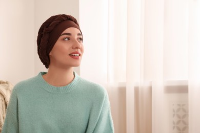 Cancer patient. Young woman with headscarf near window indoors, space for text