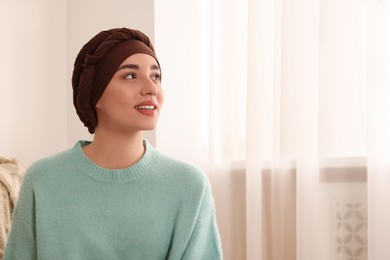 Photo of Cancer patient. Young woman with headscarf near window indoors, space for text