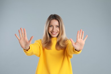 Photo of Woman showing number ten with her hands on light grey background