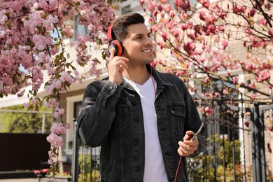 Happy man with smartphone listening to audiobook outdoors on spring day