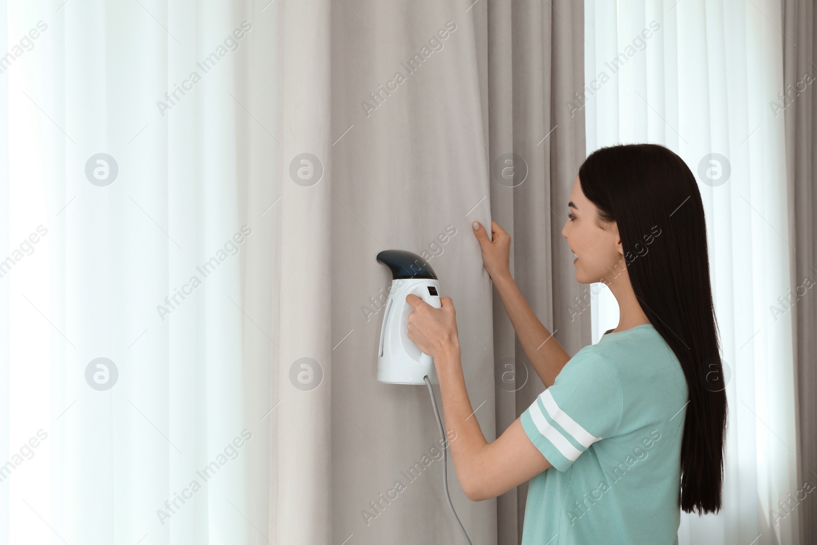 Photo of Woman steaming curtain near window at home. Space for text