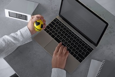 Photo of Woman squeezing antistress ball while working on laptop at table, above view