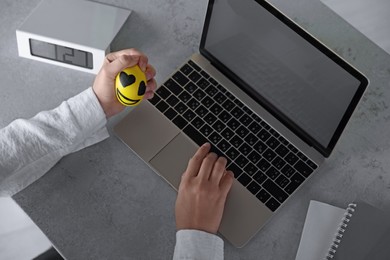 Woman squeezing antistress ball while working on laptop at table, above view