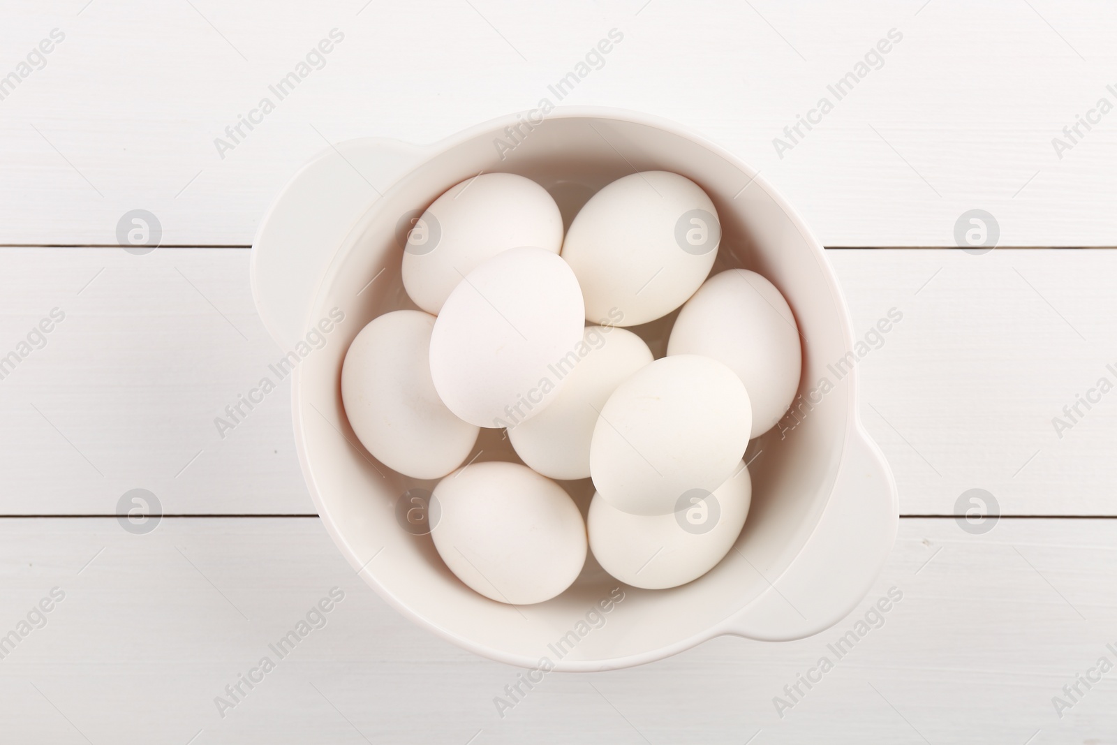 Photo of Boiled eggs in saucepan on white wooden table, top view