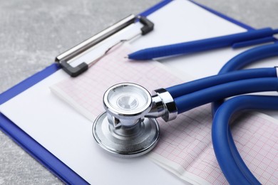 Photo of Clipboard with stethoscope and cardiogram on grey table, closeup