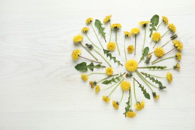 Photo of Heart made of beautiful yellow dandelions on white wooden table, flat lay. Space for text