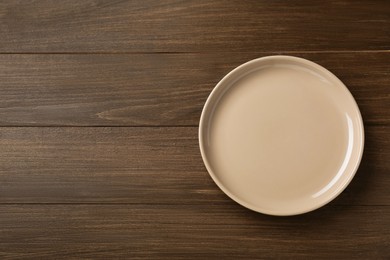 Clean beige plate on wooden table, top view. Space for text