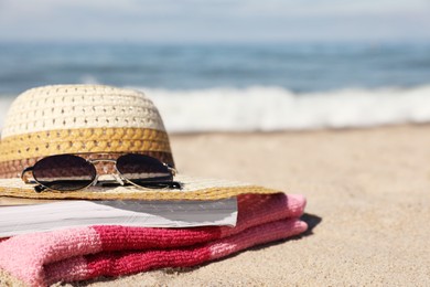 Photo of Hat, sunglasses, book and striped towel on sandy beach near sea, closeup. Space for text