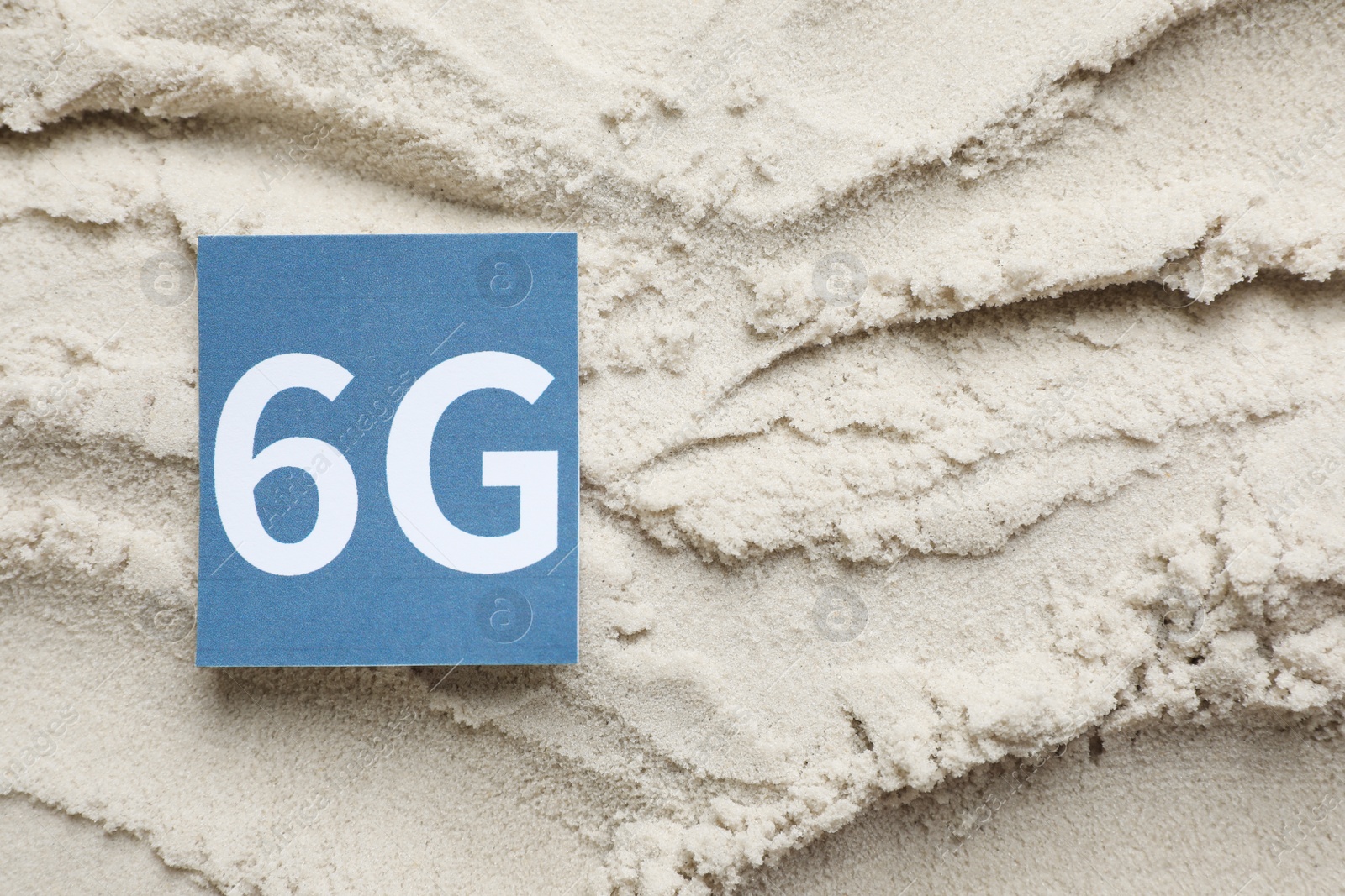 Photo of 6G technology, Internet concept. Card on white sand, top view. Space for text