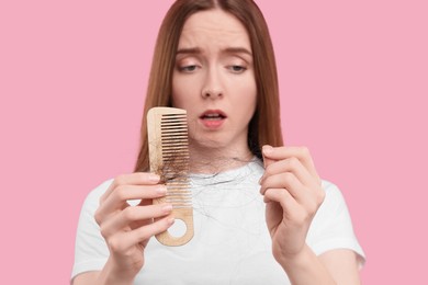 Emotional woman untangling her lost hair from comb on pink background, selective focus. Alopecia problem