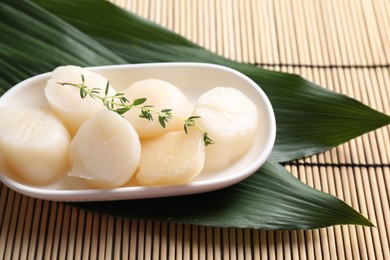 Photo of Fresh raw scallops, thyme and green leaves on bamboo mat, closeup